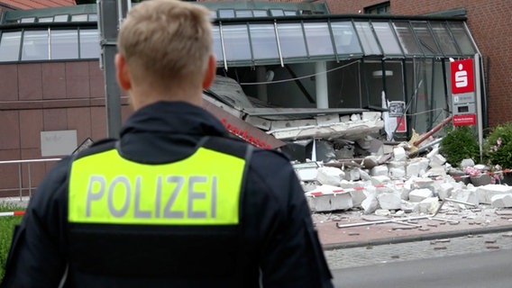 Ein Polizist steht vor einem bei einer Geldautomatensprengung stark beschädigten Sparkassengebäude in Edewecht. © Telenewsnetwork 