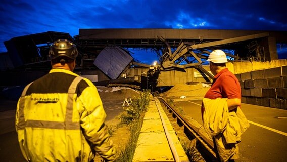 Zwei Arbeiter stehen vor der Umschlagbrücke am Emder Südkai nach der Sprengung. © dpa-Bildfunk Foto: Sina Schuldt