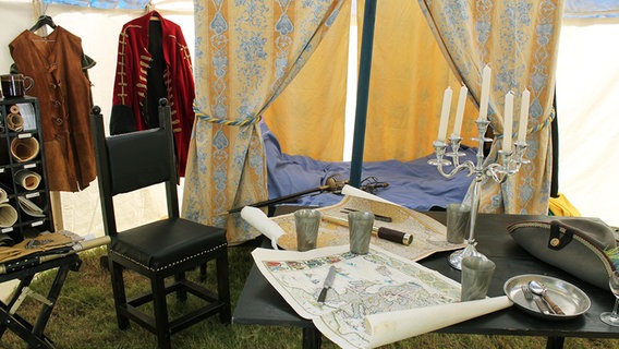 Ein antikes Bett und Tisch stehen in einem Zelt. © Landesmuseum Emden 