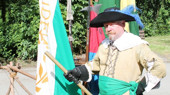 Ein Mann posiert mit Hut vor bunten Fahnen. © Landesmuseum Emden 