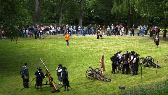 Auf einer Wiese stehen historisch gekleidete Personen neben Kanonen und anderen mittelalterlichen Waffen. © dpa - Bildfunk Foto: Carmen Jaspersen