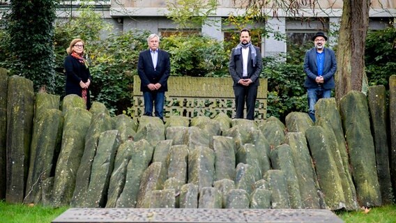 Christiane Cordes, Amtsleiterin im Amt für Kultur, Museen und Sport, Dietmar Schütz, Vorsitzender der Oldenburger Bürgerstiftung, Maximilian Strnad, Mitarbeiter in der Koordinierungsstelle Erinnerungszeichen bei der Stadt München, und Farschid Ali Zahedi, Gründer des Vereins Werkstattfilm, stehen an einem Mahnmal für die Opfer des Nationalsozialismus im Stadtzentrum von Oldenburg. © dpa Foto: Hauke-Christian Dittrich