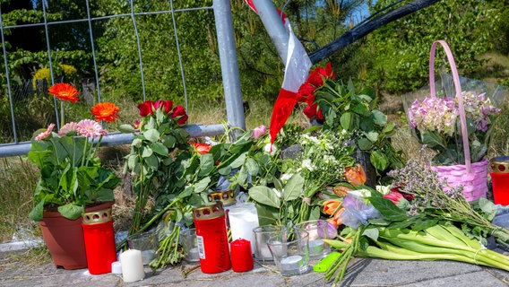 Auf dem Bild sind Kerzen, Blumen und ein Absperrband der Polizei an einem Weg zu sehen. An der Stelle soll ein Mann seine Ehefrau absichtlich überfahren haben. © dpa-Bildfunk Foto: Sina Schuldt