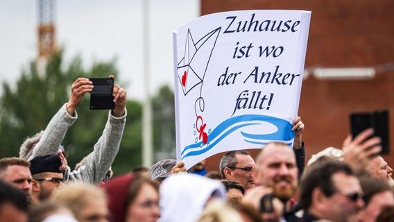 Angehörige von Besatzungsmitgliedern warten bei Rückkehr der Fregatte "Brandenburg" (F215) aus dem Mittelmeer mit einem Plakat mit der Aufschrift "Zuhause ist wo der Anker fällt!" auf dem Kai. © dpa Foto: Focke Strangmann
