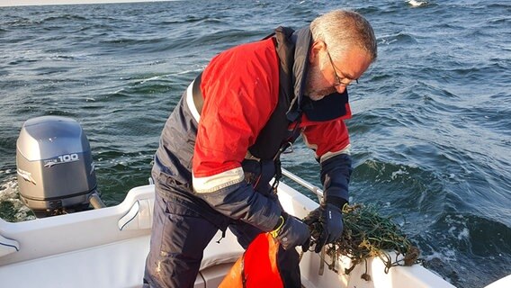 Ein Mann zieht ein Fischernetz in ein Schlauchboot. © Ghost Diving Germany 