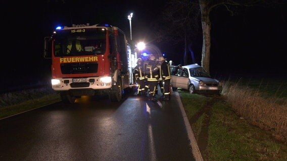 Ein beschädigtes Auto steht nach einem Unfall an einem Baum, Einsatzkräfte der Feuerwehr sind zugegen. © NonstopNews 