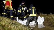 Einsatzkräfte der Feuerwehr sichern in Verden einen Deich mit Sandsäcken. © Nord-West-Media TV 