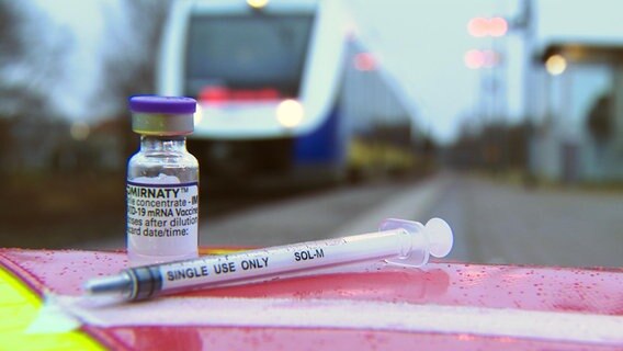 Eine Spritze und Impfstoff vor einem Zug der Nordwestbahn. © NDR 