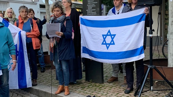 Eine Frau spricht auf einer Kundgebung anlässlich des Krieges in Israel. Daneben eine Flagge Israels. © NDR Foto: Annete Laug