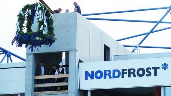 An einem unfertigen Gebäude hängt ein großer Richtkranz und ein Banner mit der Aufschrift "Nordfrost". © NDR Foto: Ursula Mueller