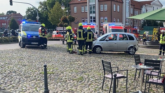 Einsatzfahrzeuge und -kräfte der Feuerwehr, Polizei und Rettungswagen stehen auf einem Marktplatz um einen Pkw herum. © Polizeiinspektion Wilhelmshaven/Friesland 