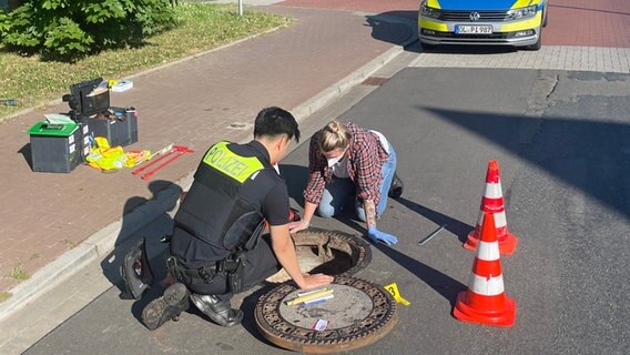 Eine Polizistin und ein Polizist knien vor einem geöffneten Gullydeckel. © Andre van Elten/dpa Foto: Andre van Elten