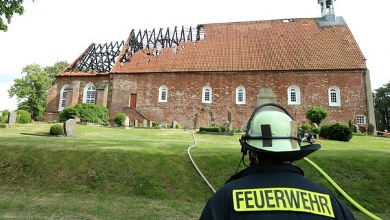 Ein Feuerwehrmann steht neben der St.-Bartholomäus-Kirche. © picture alliance/dpa/Polizei Delmenhorst | Polizei Delmenhorst Foto: Polizei Delmenhorst