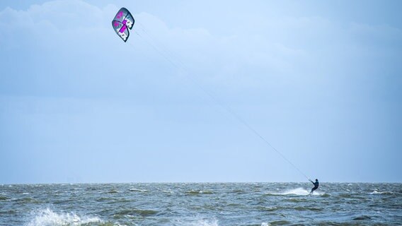 Ein Windsurfer und mehrere Kitesurfer fahren durch das spritzende Wasser der Nordsee. © dpa-Bildfunk Foto: Sina Schuldt