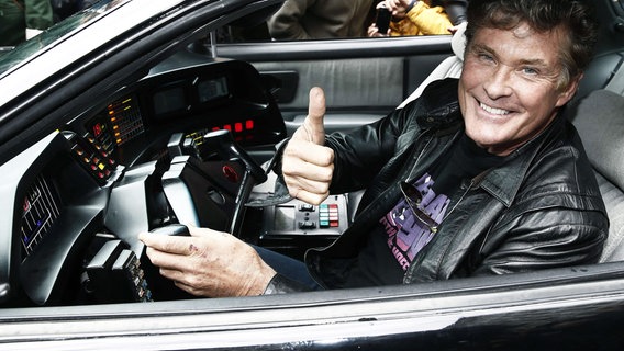 Schauspieler David Hasselhoff sitzt in seinem K.I.T.T.-Wagen, das er in seiner früheren Rolle in der Serie "Knight Rider" gefahren hat und hält den Daumen nach oben. © dpa picture alliance Foto: Jesus Diges