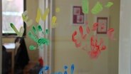 Farbige Handabdrücke und Namen von Kindern an einer Glasscheibe. © NDR Foto: Jessica Becker