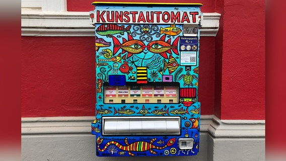 EIn Bunter Automat mit der Aufschrift "Kunstautomat" hängt an einer roten Hauswand. © NDR Foto: Jutta Przygoda