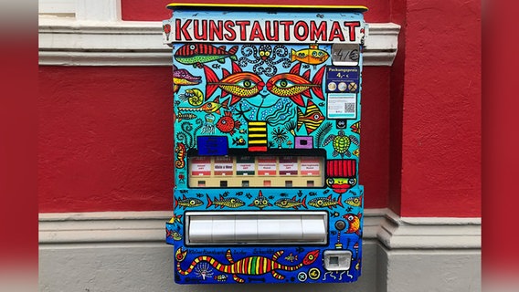 EIn Bunter Automat mit der Aufschrift "Kunstautomat" hängt an einer roten Hauswand. EIn Bunter Automat mit der Aufschrift "Kunstautomat" hängt an einer roten Hauswand. © NDR Foto: Jutta Przygoda