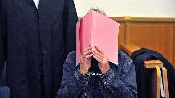 Der Angeklagte verdeckt sein Gesicht mit einer Aktenmappe. © picture alliance / dpa Foto: Carmen Jaspersen