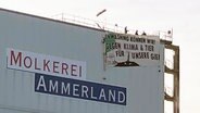 Aktivisten von "Animal Rebellion" hängen ein Banner mit den Worten "Greenwashing können wir! Gegen Klima & Tier für unsere Gier" an einem Gebäude der Molkerei Ammerland auf. © NDR Foto: Olaf Kretschmer