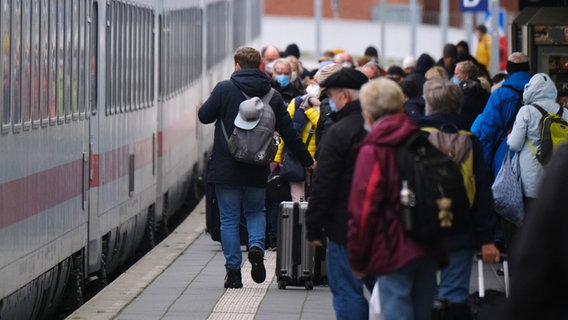 Menschen stehen auf einem Bahnsteig am Bahnhof Norddeich Mole vor einem eingefahrenen Zug. © picture alliance/dpa Foto: Markus Hibbeler