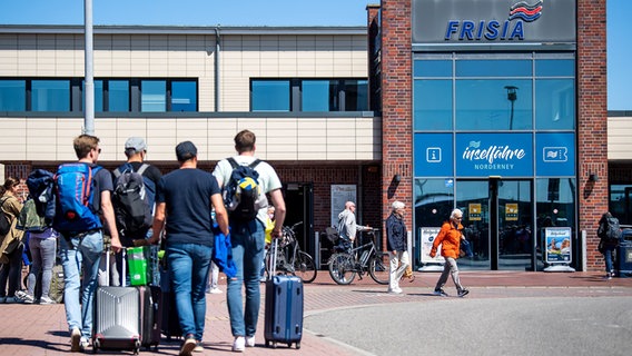 Reisende mit Gepäck laufen zur Fähre. Die Reederei Norden-Frisia setzt angesichts des hohen Anreiseaufkommens zusätzliche Fähren ab Norddeich ein. © Sina Schuldt/dpa Foto: Sina Schuldt