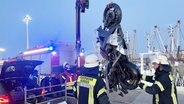 Feuerwehrleute heben mit einem Kran ein Motorrad aus dem Hafen in Norddeich. © Feuerwehr Norden 