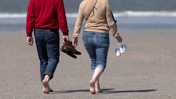 Zwei Personen laufen barfuß über einen Strand und tragen ihre Schuhe in den Händen. © dpa - Bildfunk Foto: Janis Meyer