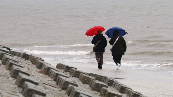 Spaziergängerinnen gehen mit Regenschirmen am Nordstrand der ostfriesischen Insel Norderney bei regnerischem Wetter. © dpa-Bildfunk Foto: Volker Bartels