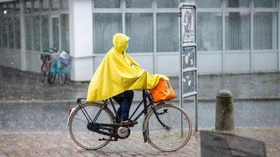 Ein Frau fährt während eines Gewitters mit einem gelben Regenponcho durch Oldenburg. © dpa-Bildfunk Foto: Hauke-Christian Dittrich