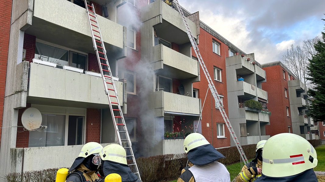 Einsatzkräfte der Feuerwehr stehen vor einem brennenden Mehrfamilienhaus in Osterholz-Scharmbeck.