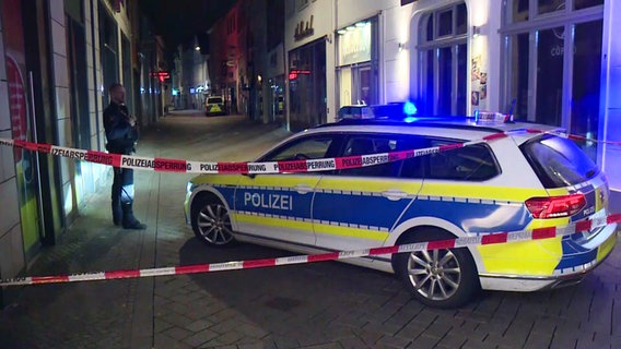 Ein Polizeiauto steht hinter einer Absperrung in auf einer engen Straße. Polizei-Abklebeband klebt am Auto, ein Beamter in Uniform steht vor einem Haus. © NonstopNews 