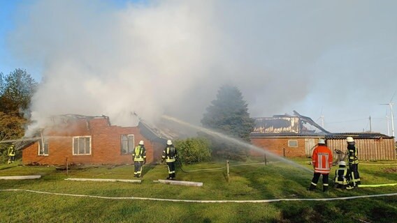 Feuerwehrleute löschen ein brennendes Haus. © Nord-West-Media TV/dpa 