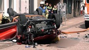 Feuerwehrleute an einem Auto, das nach einem Sturz aus einem Parkhaus auf dem Dach liegt. © NonstopNews 