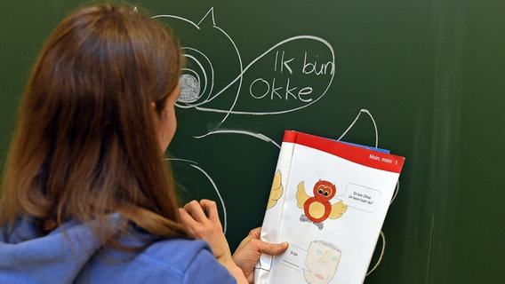 Eine Lehrerin steht in Wallhöfen vor einer Tafel im Plattdeutsch-Unterricht und hat "Ik bünn okke" in die Sprechblase einer Eule geschrieben. © dpa - Bildfunk Foto: Carmen Jaspersen