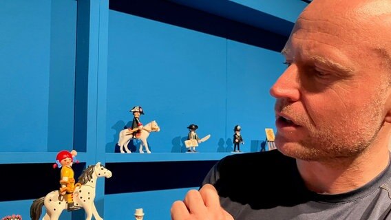 Ausstellungsmacher Hamburger Oliver Schaffer hält eine Playmobilfigur in einer Ausstellung im Deutschen Pferdemuseum in den Händen. © NDR Foto: Maren Momsen