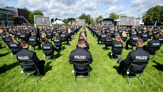 Polizistinnen und Polizisten des Bachelorstudienjahrgangs der Polizeiakademie Niedersachsen sitzen bei ihrer Abschlussfeier auf einem Sportplatz. © dpa-Bildfunk Foto: Hauke-Christian Dittrich