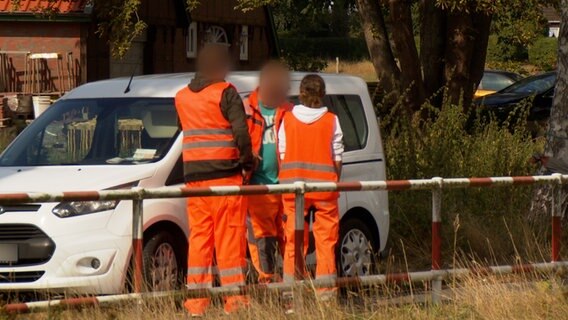 Drei Personen in Signalkleidung stehen an einem Auto an einem Bahnübergang. © NDR 