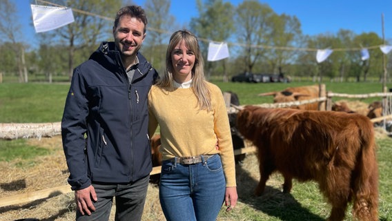 Ein Mann und eine Frau stehen neben Hochlandrindern. © NDR Foto: Catherine Grim