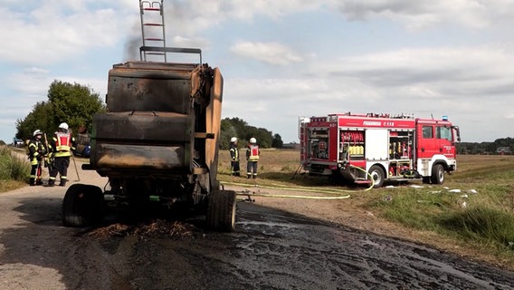 Eine verkohlte Rundballenpresse steht nach einem Feuer auf einem Feld in Syke. © Nord-West-Media TV 