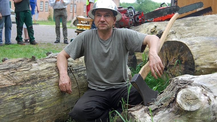 Peter Schlicht sitzt neben einer Holzaxt. © NDR Fotograf: Carsten Valk