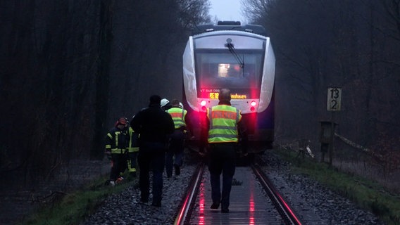 Einsatzkräfte der Feuerwehr stehen vor einem Regionalzug auf einer Bahnstrecke bei Sandkrug. © NonstopNews 