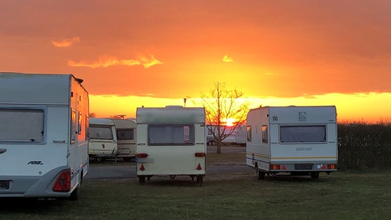 Von einem Campingplatz mit Wohnwagen aus ist ein Sonnenaufgang zu beobachten. © NDR Foto: Jutta Przygoda