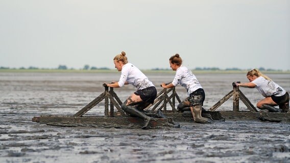 Teilnehmerinnen der Deutschen Meisterschaft im Schlickrutschen rutschen am Kurhausstrand in Dangast durch den Schlick. © Markus Hibbeler/dpa Foto: Markus Hibbeler