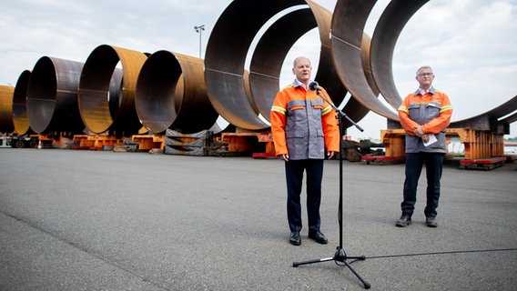 Bundeskanzler Olaf Scholz (l, SPD) spricht vor Journalisten, während er gemeinsam mit Andreas Liessem, Geschäftsführer von Steelwind Nordenham GmbH, vor zahlreichen Bauteilen für die Stahlfundamente von Windkraftanlagen steht. © dpa-Bildfunk Foto: Hauke-Christian Dittrich