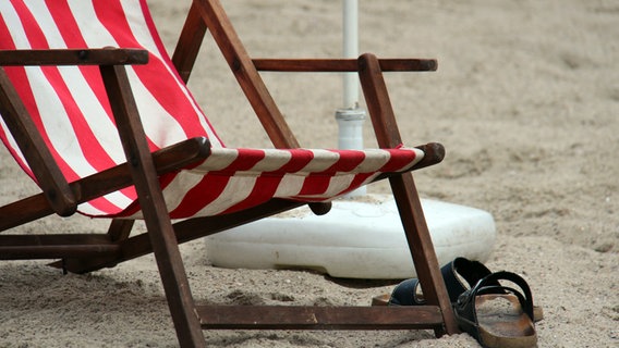 Ein Liegestuhl und Schlappen liegen auf Sand. © NDR Foto: Andreas Barnickel
