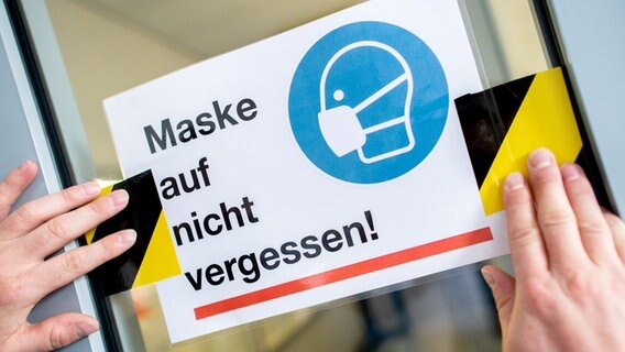 Ein Schild mit der Aufschrift "Maske auf nicht vergessen!" wird an einer Tür befestigt. © dpa-Bildfunk Foto: Hauke-Christian Dittrich