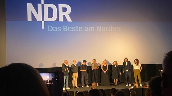 Mitwirkende stehen bei der Premiere des Films "Sörensen fängt Feuer" auf der Bühne vor der Kino-Leinwand. © NDR Foto: Marlene Santel