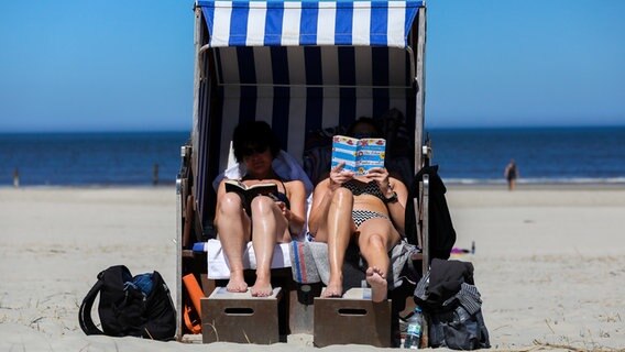 Zwei Frauen liegen bei schönem Wetter in einem Strandkorb und lesen. © dpa-Bildfunk Foto: Mohssen Assanimoghaddam