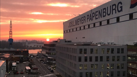 Die Sonne geht am frühen Morgen hinter dem Hauptgebäude der Meyer Werft in Papenburg auf.  Foto: Oliver Gressieker
